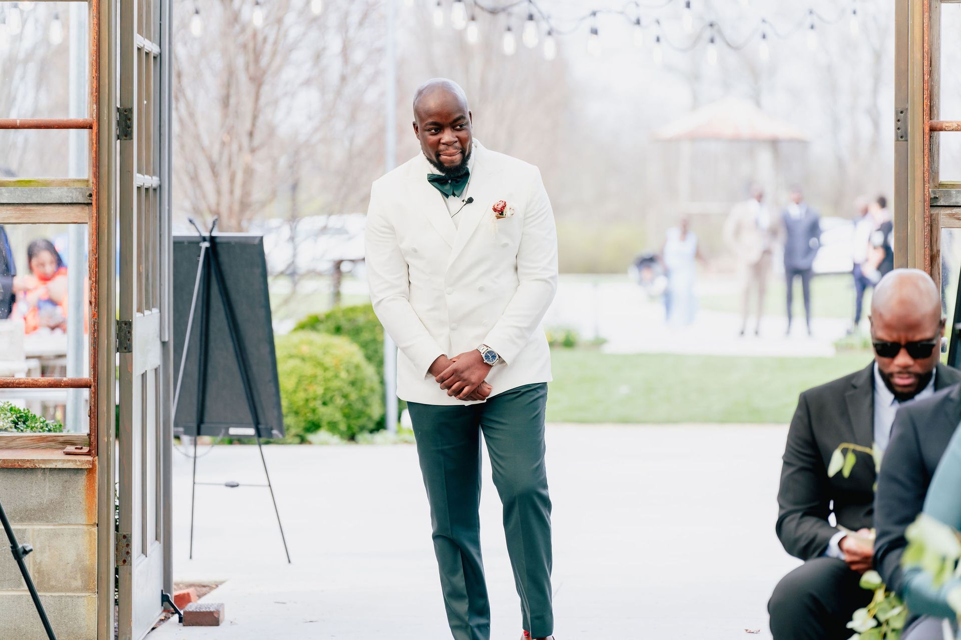 A man in a white suit is walking down the aisle at a wedding.