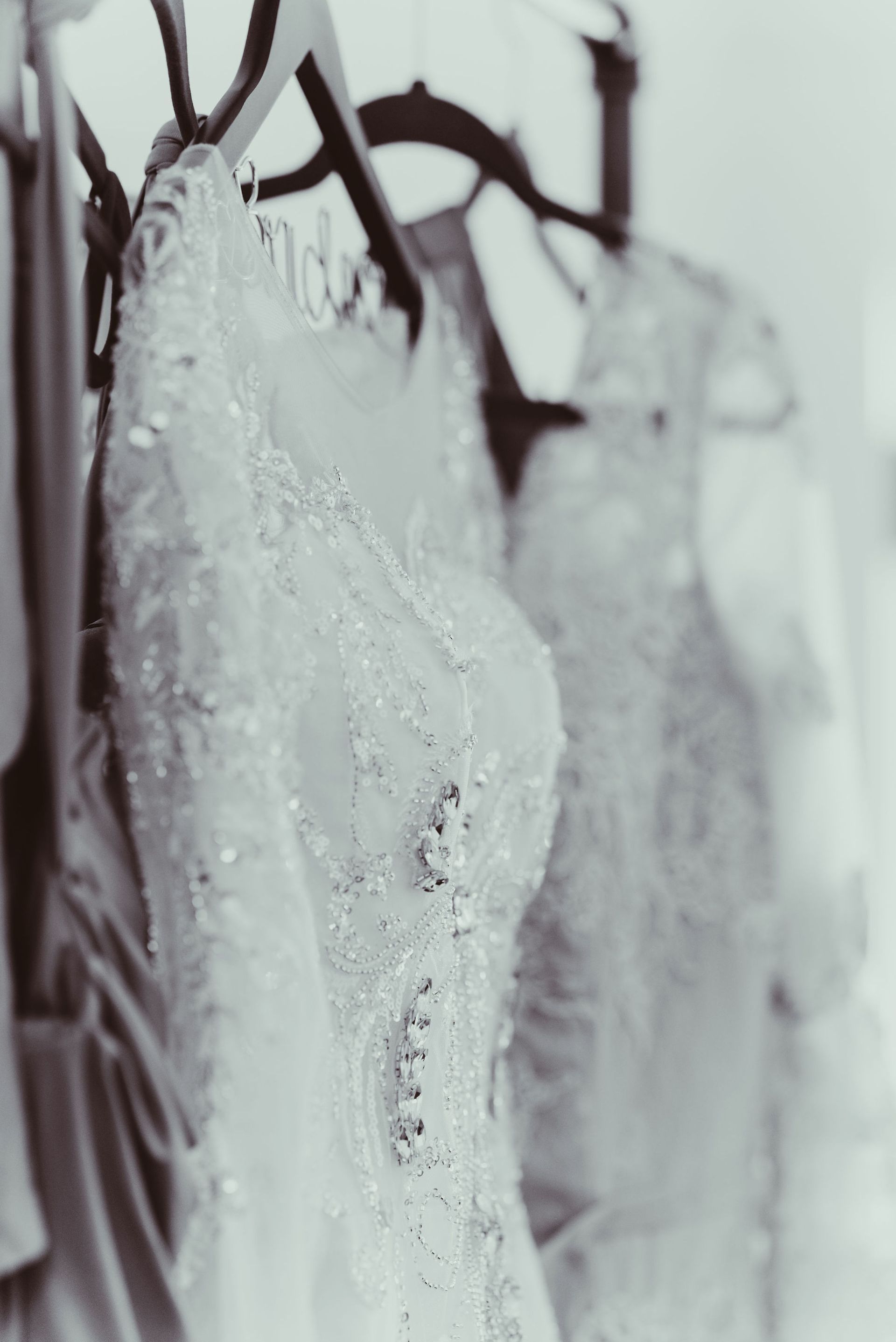 A black and white photo of a row of wedding dresses hanging on a rack.
