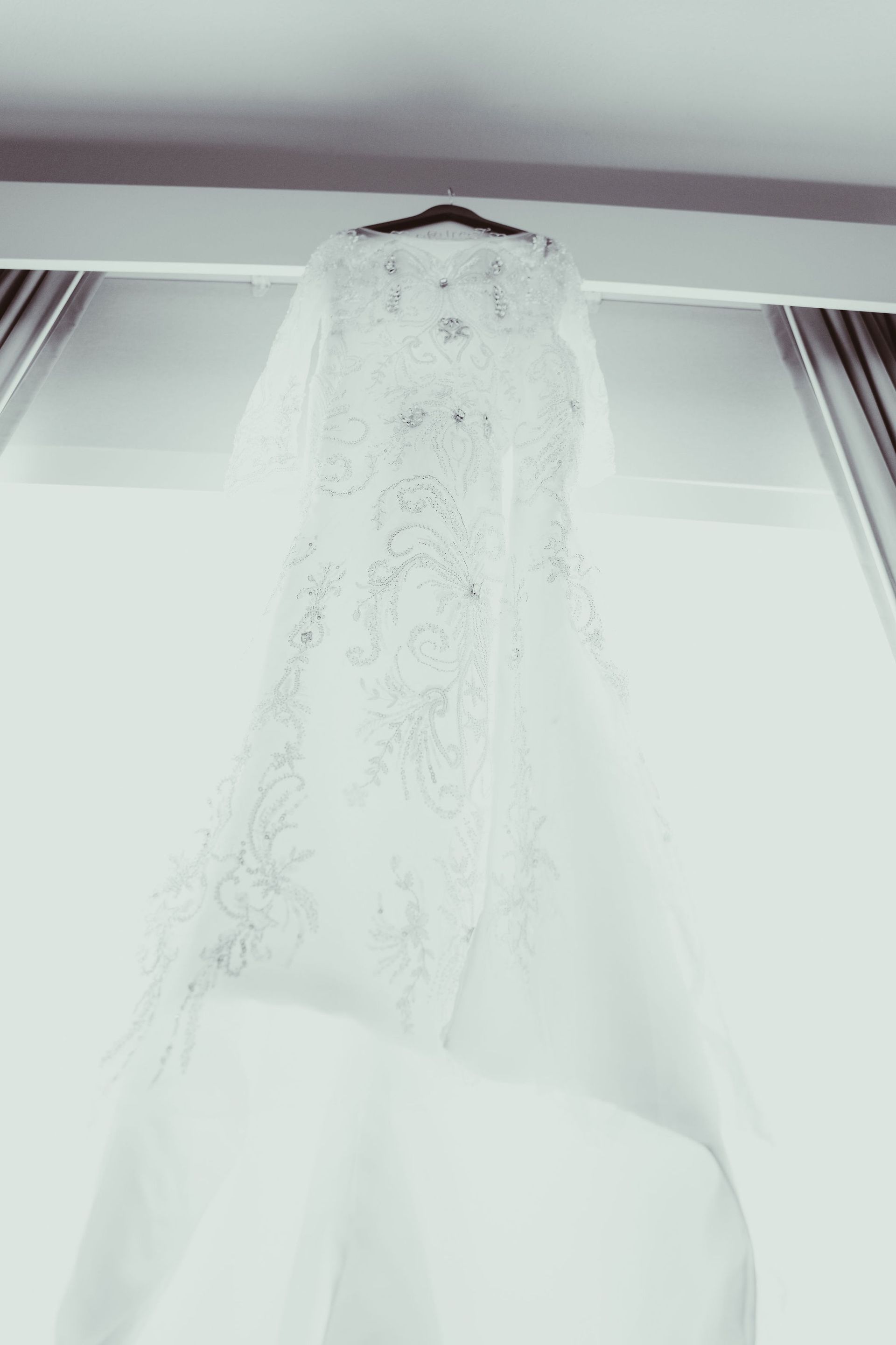 A white wedding dress with a veil is hanging from the ceiling.