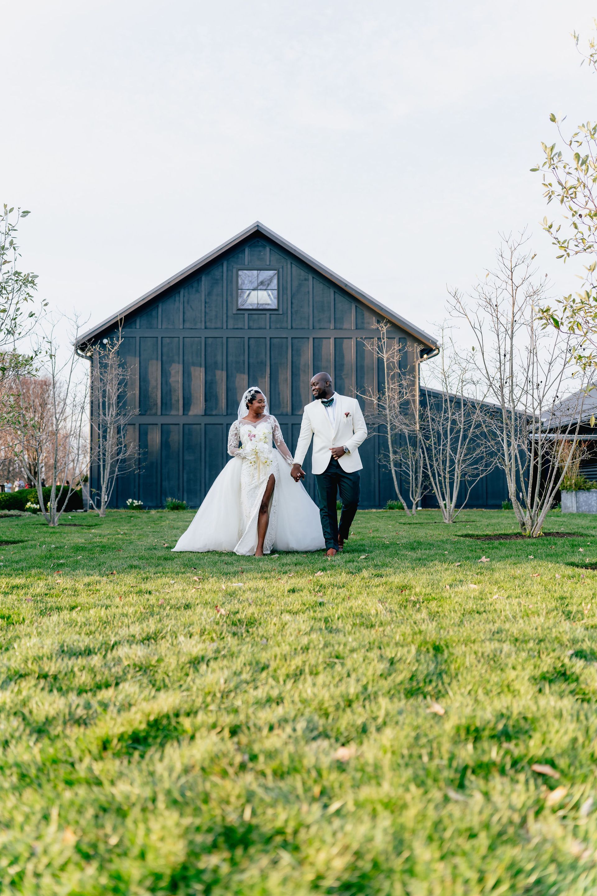 A bride and groom are walking in front of a barn holding hands.