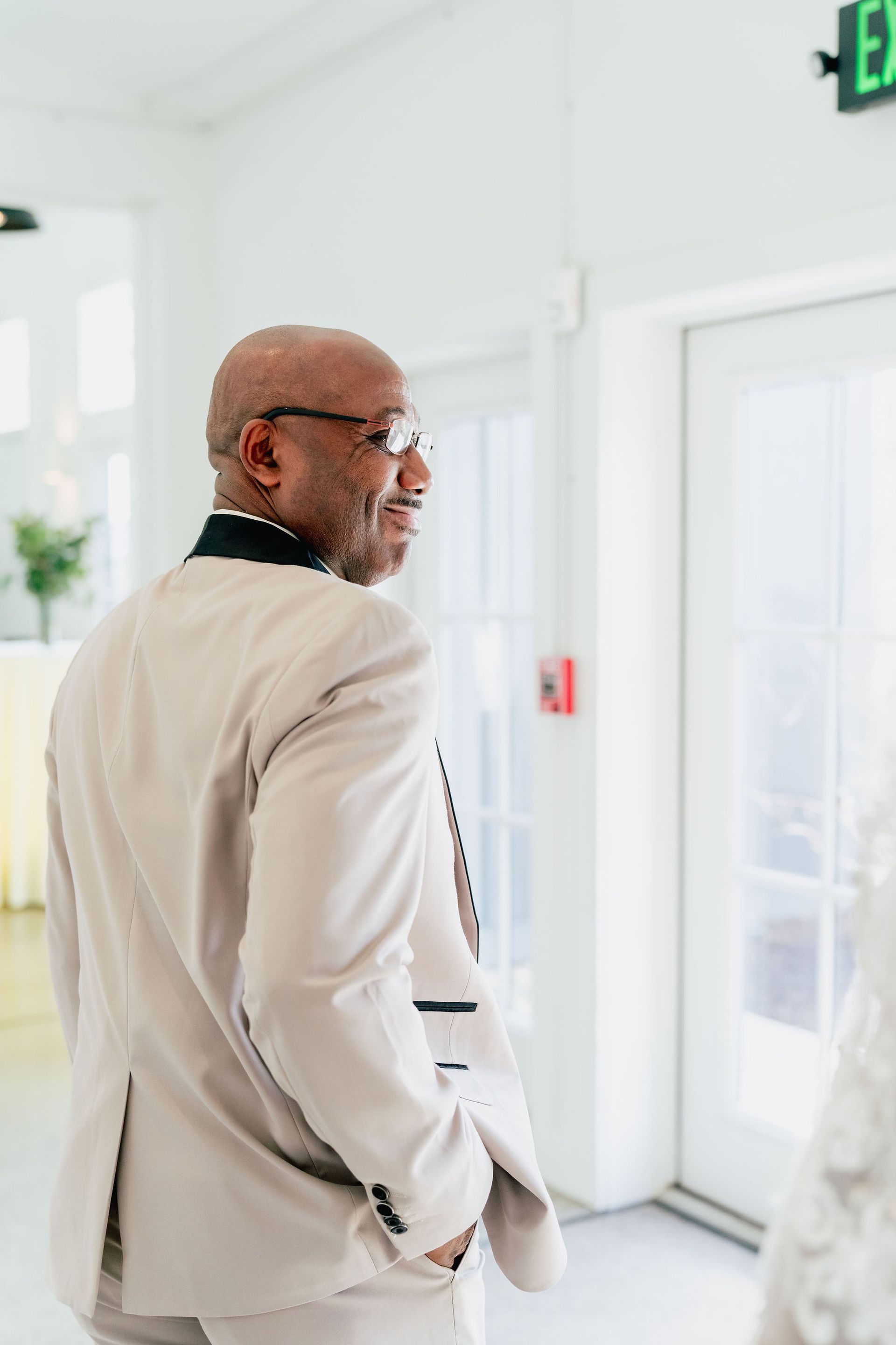 A man in a white suit is standing in a hallway with his hands in his pockets.