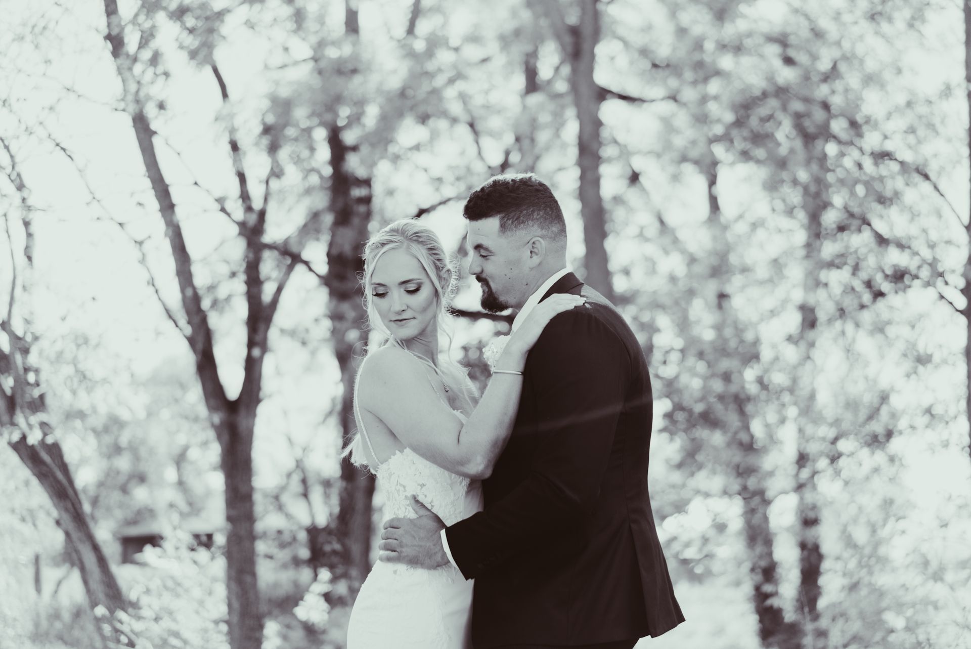 A black and white photo of a bride and groom dancing in the woods.