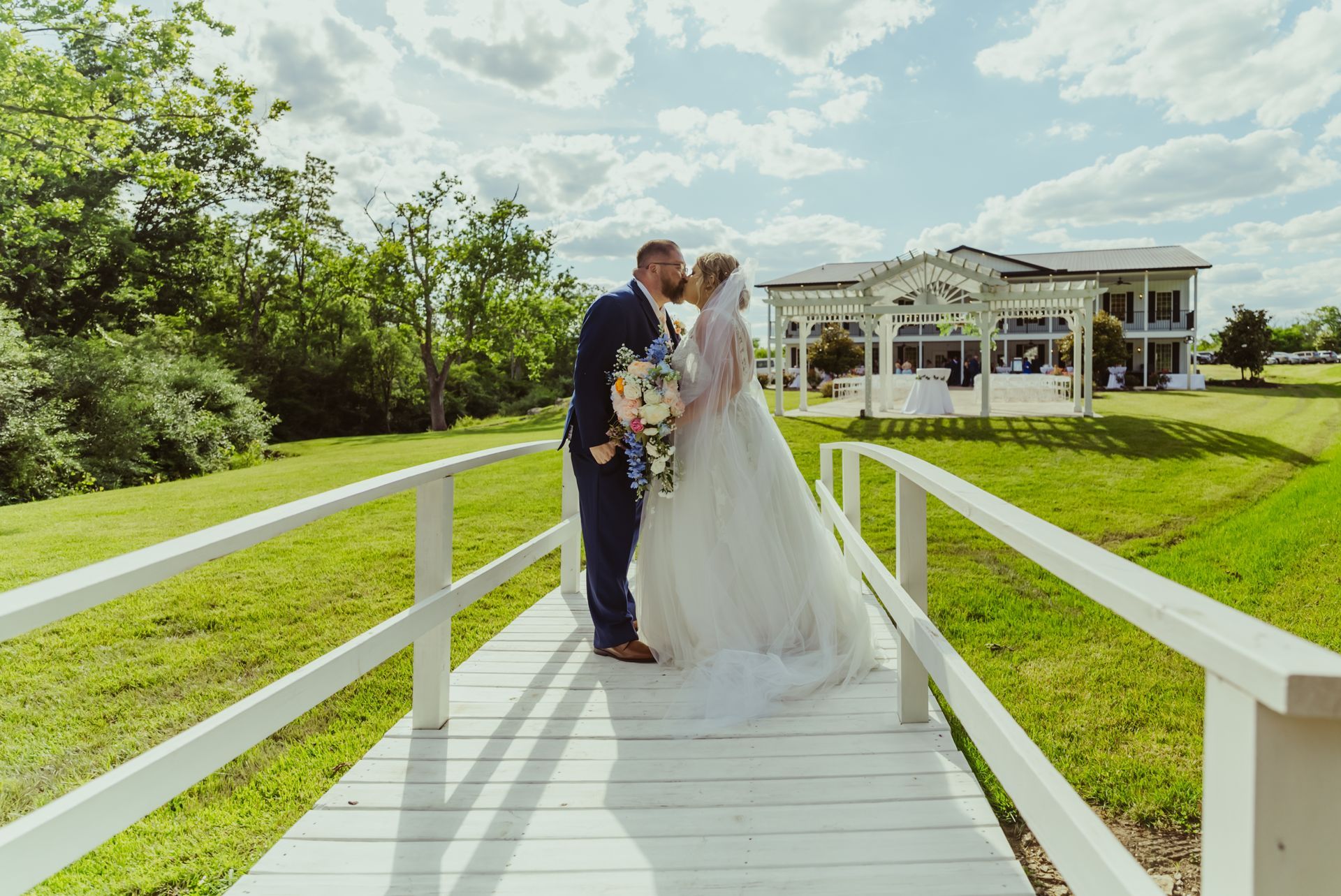 A bride and groom are kissing on a bridge in front of a house.