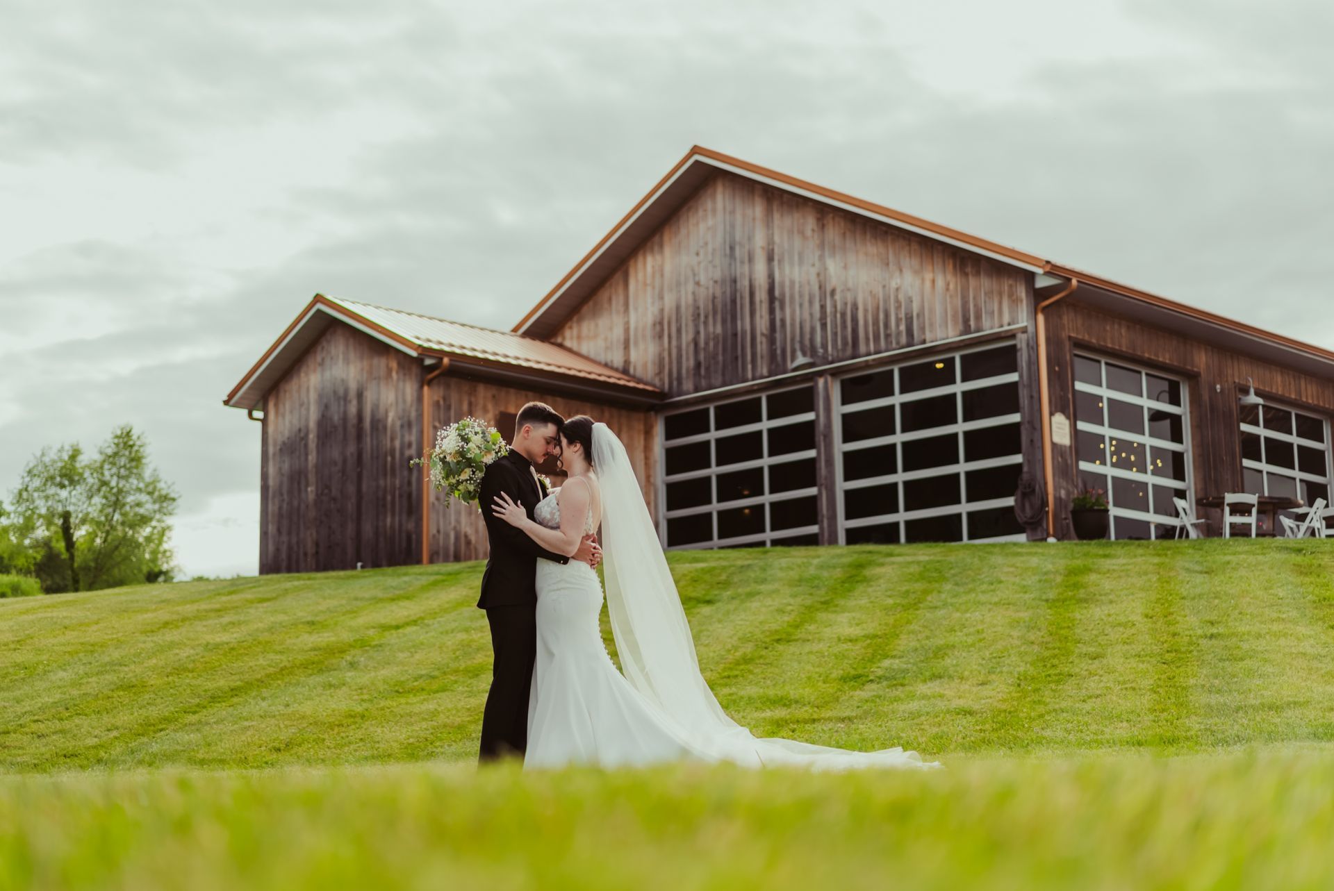 A bride and groom are posing for a picture in front of a barn.