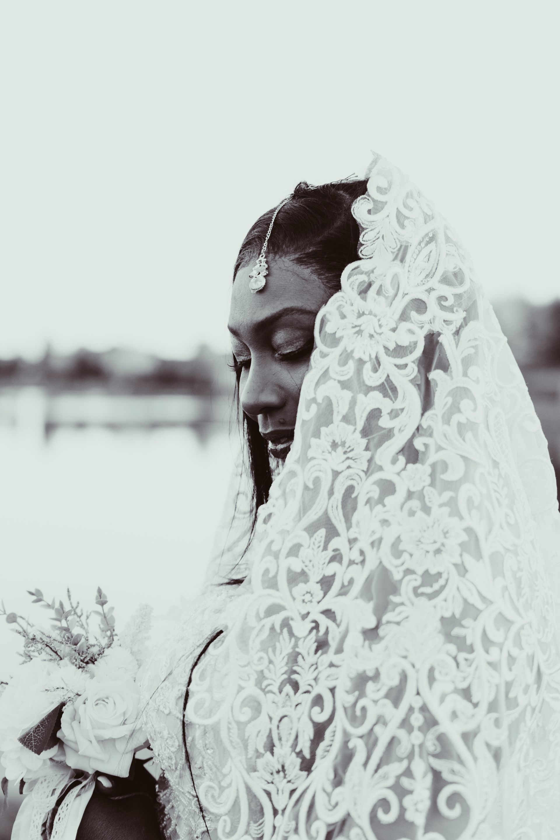 A black and white photo of a woman wearing a white lace veil.