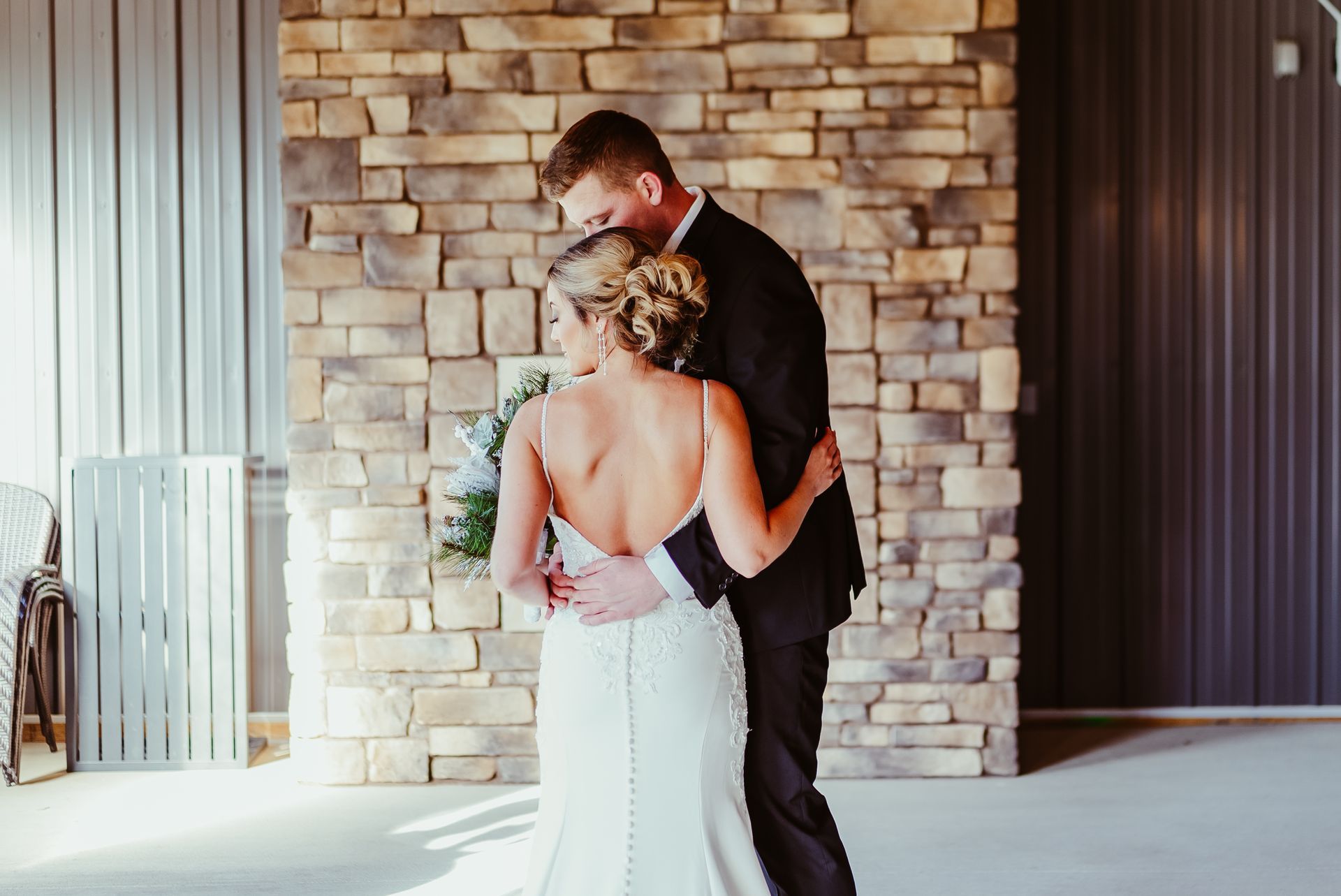 A bride and groom are hugging each other in front of a stone wall.