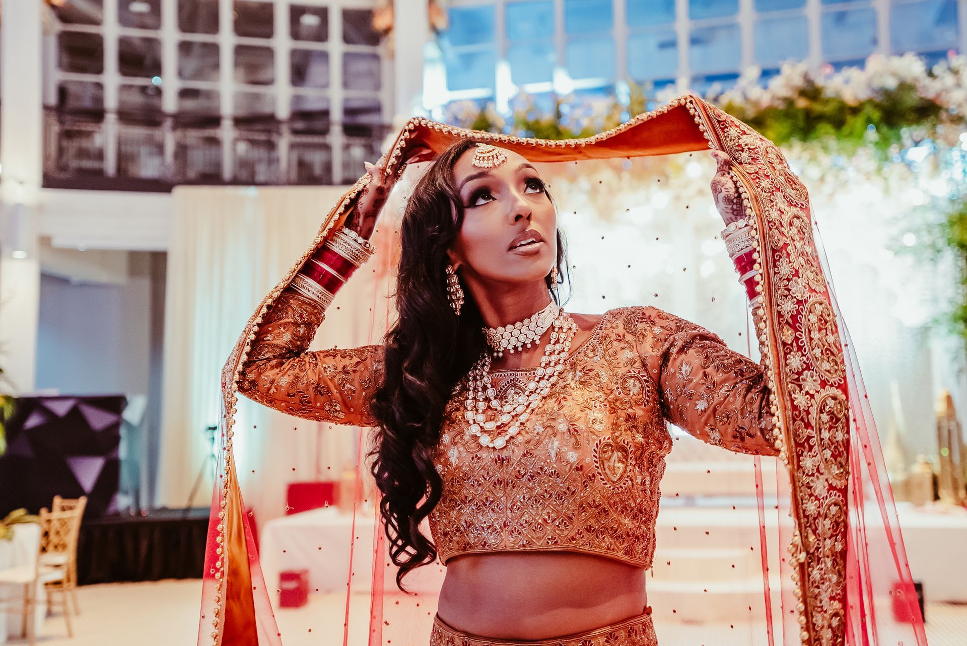 A woman in a traditional indian dress is holding a veil over her head.