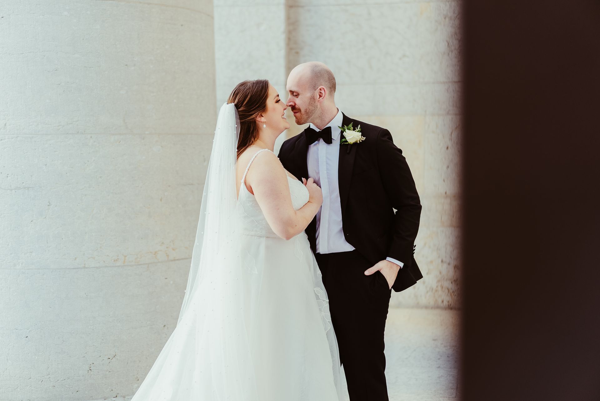 A bride and groom are kissing in front of a building.