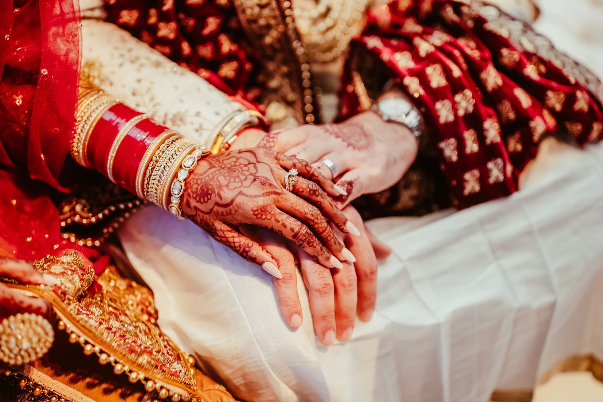 A bride and groom are holding hands while sitting on a bed.