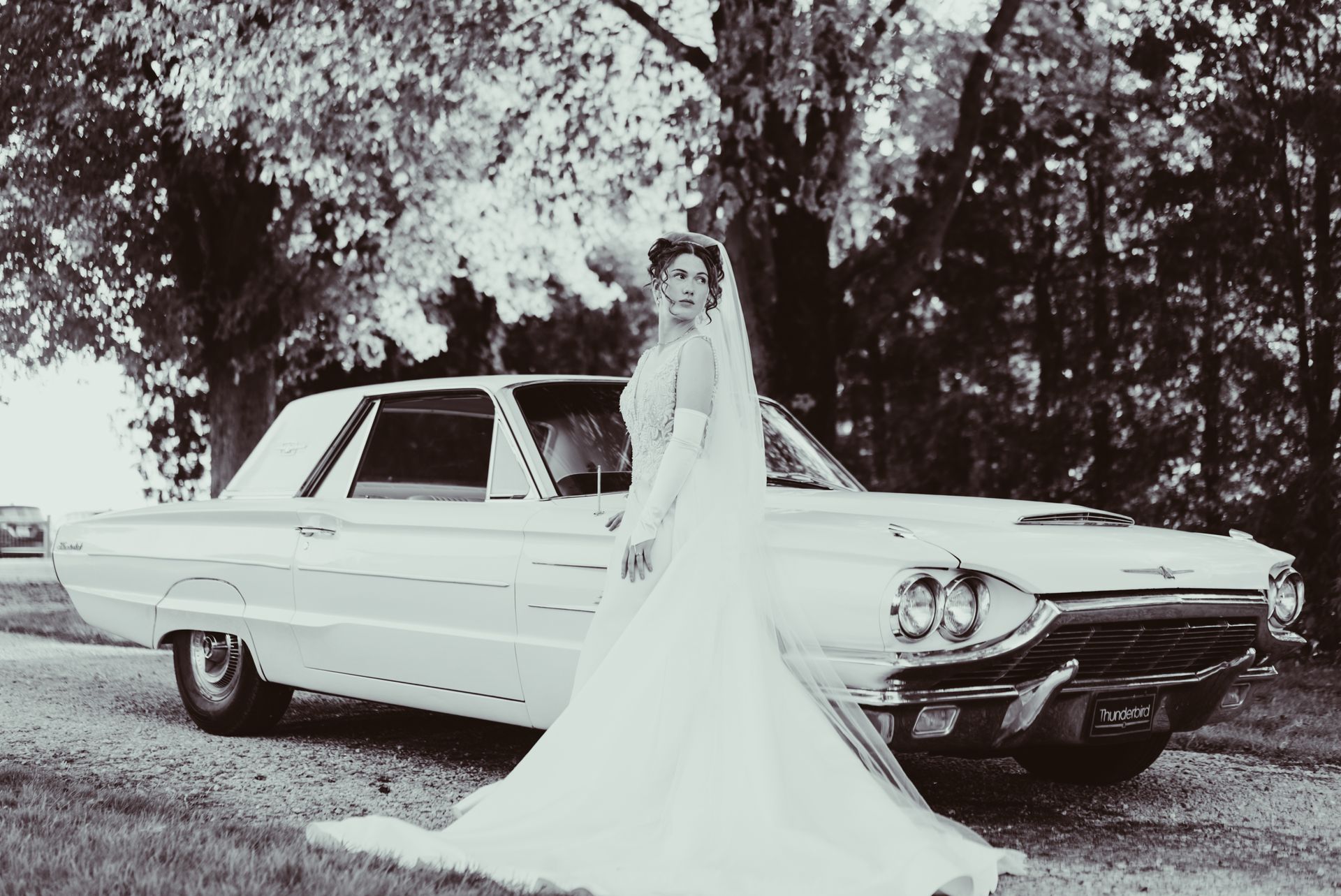 A black and white photo of a bride standing next to a white car