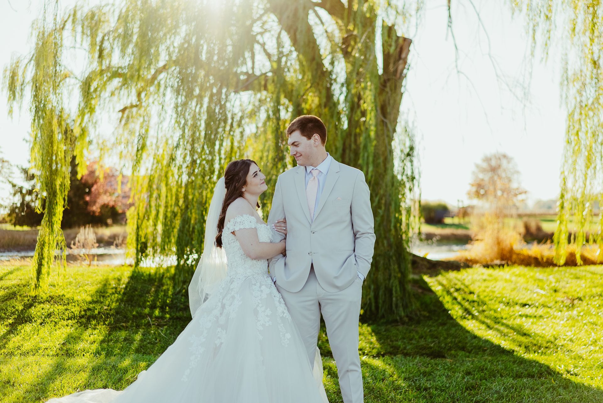 A bride and groom are posing for a picture in front of a willow tree.