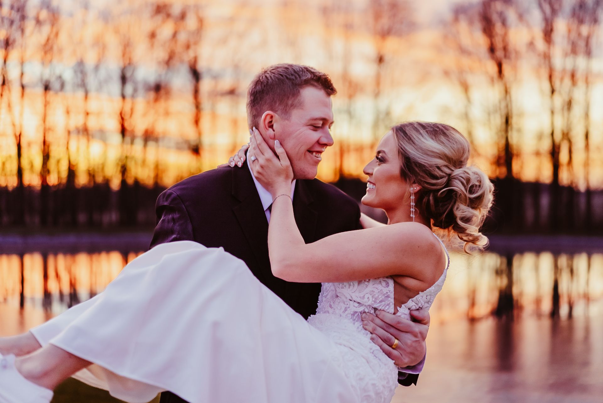 A man is carrying a bride in his arms in front of a lake.