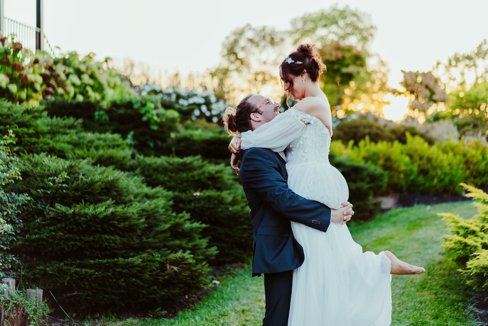 A bride and groom are posing for a picture while the groom is holding the bride in his arms.