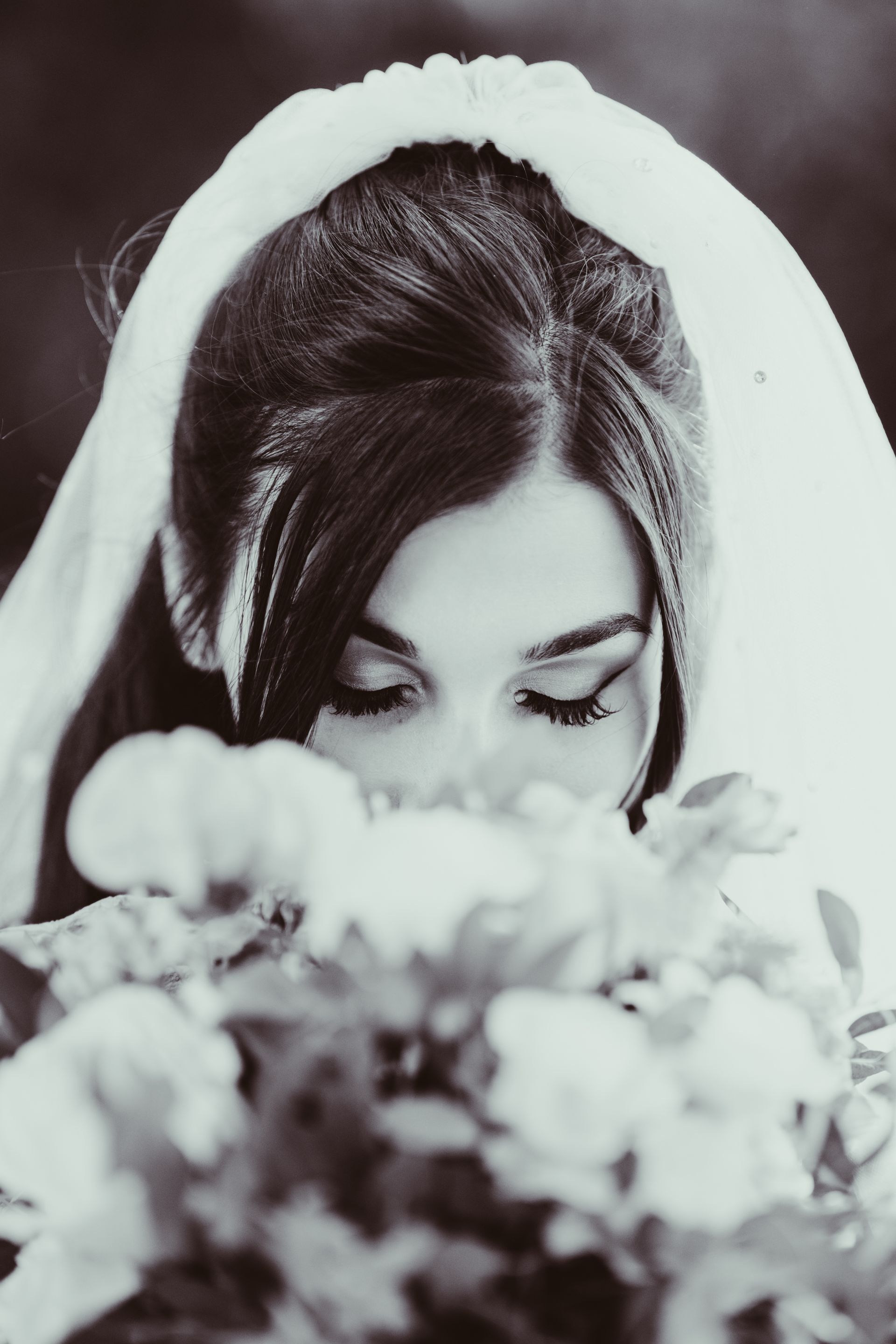 Bride with veil, looking down at bouquet, black and white.