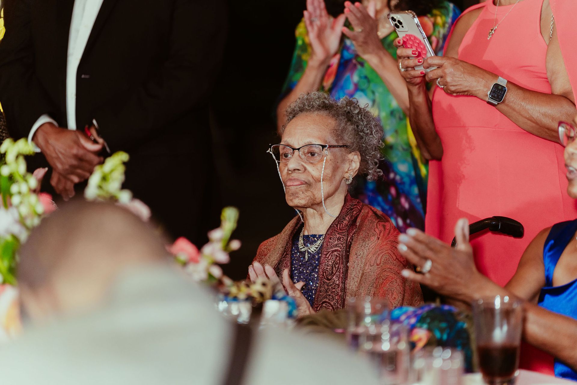 An elderly woman in a wheelchair is sitting at a table at a wedding reception.
