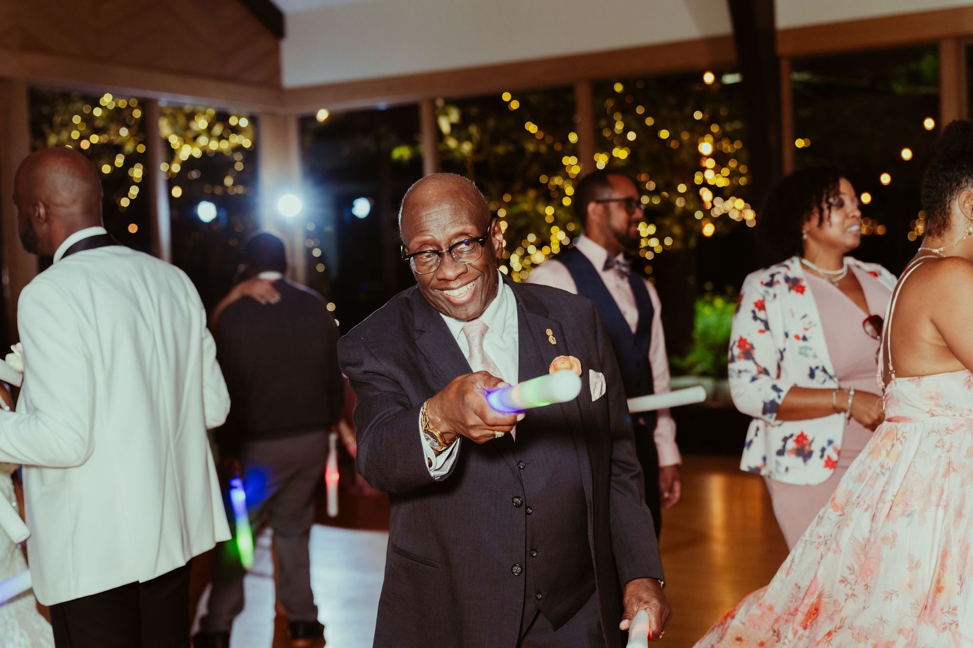 A man in a suit is holding a light stick at a wedding reception.