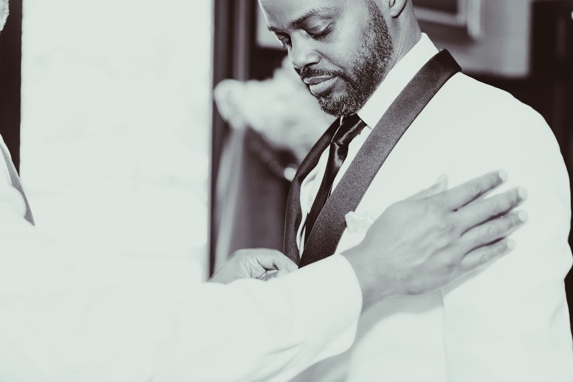 A man in a suit and tie is being helped by another man.