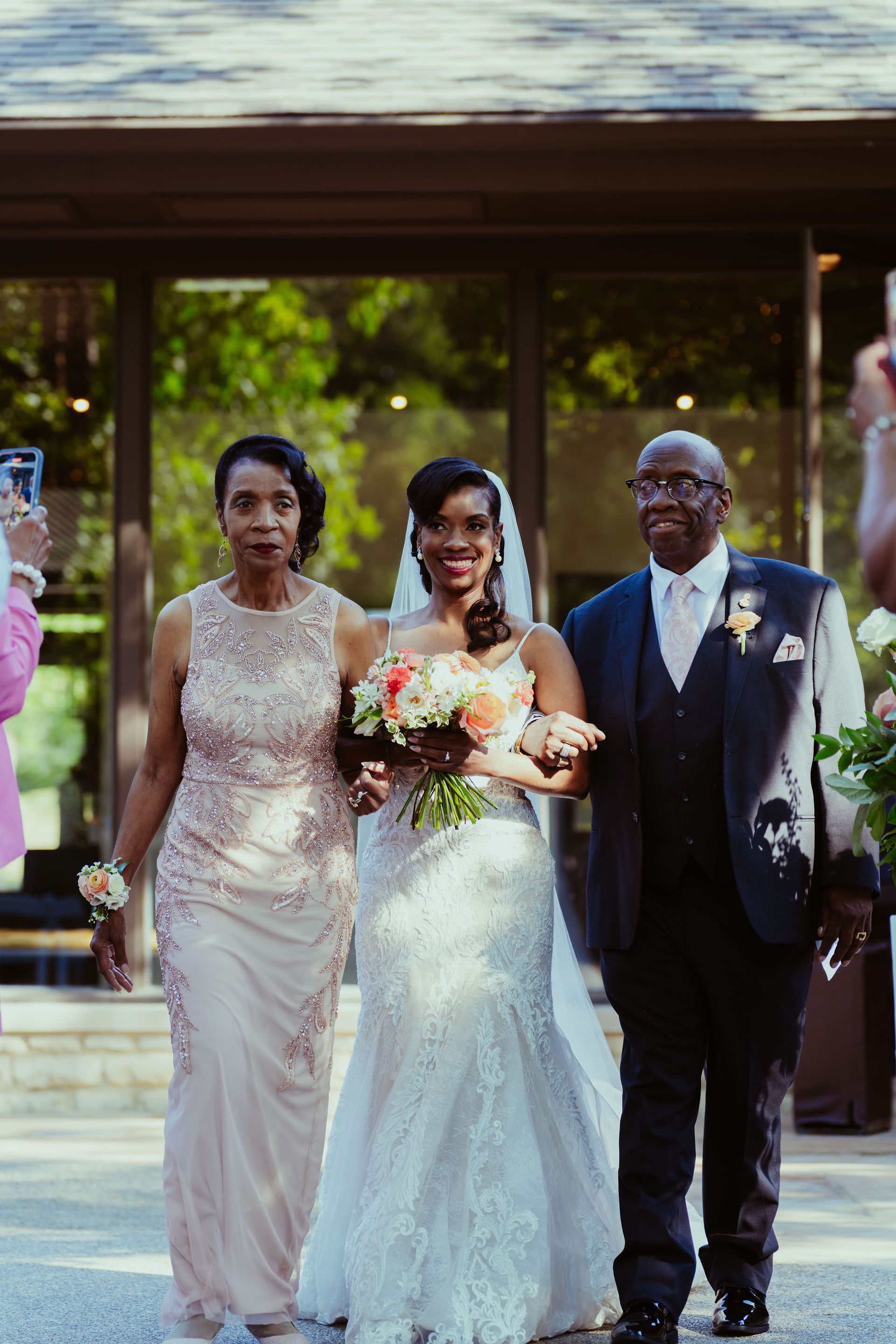 A bride is walking down the aisle with her parents at her wedding.