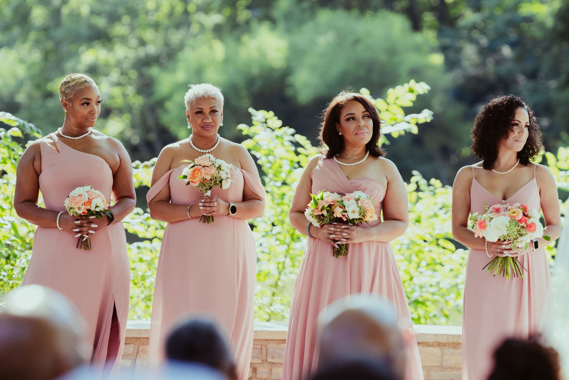 A group of women in pink dresses are standing next to each other holding bouquets of flowers.
