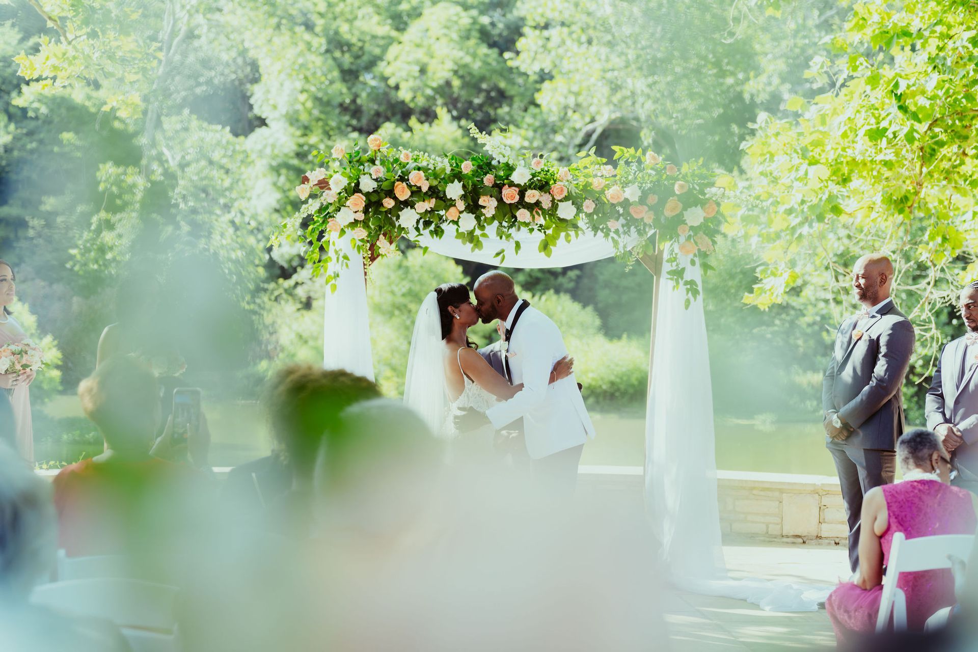 A bride and groom are kissing at their wedding ceremony.