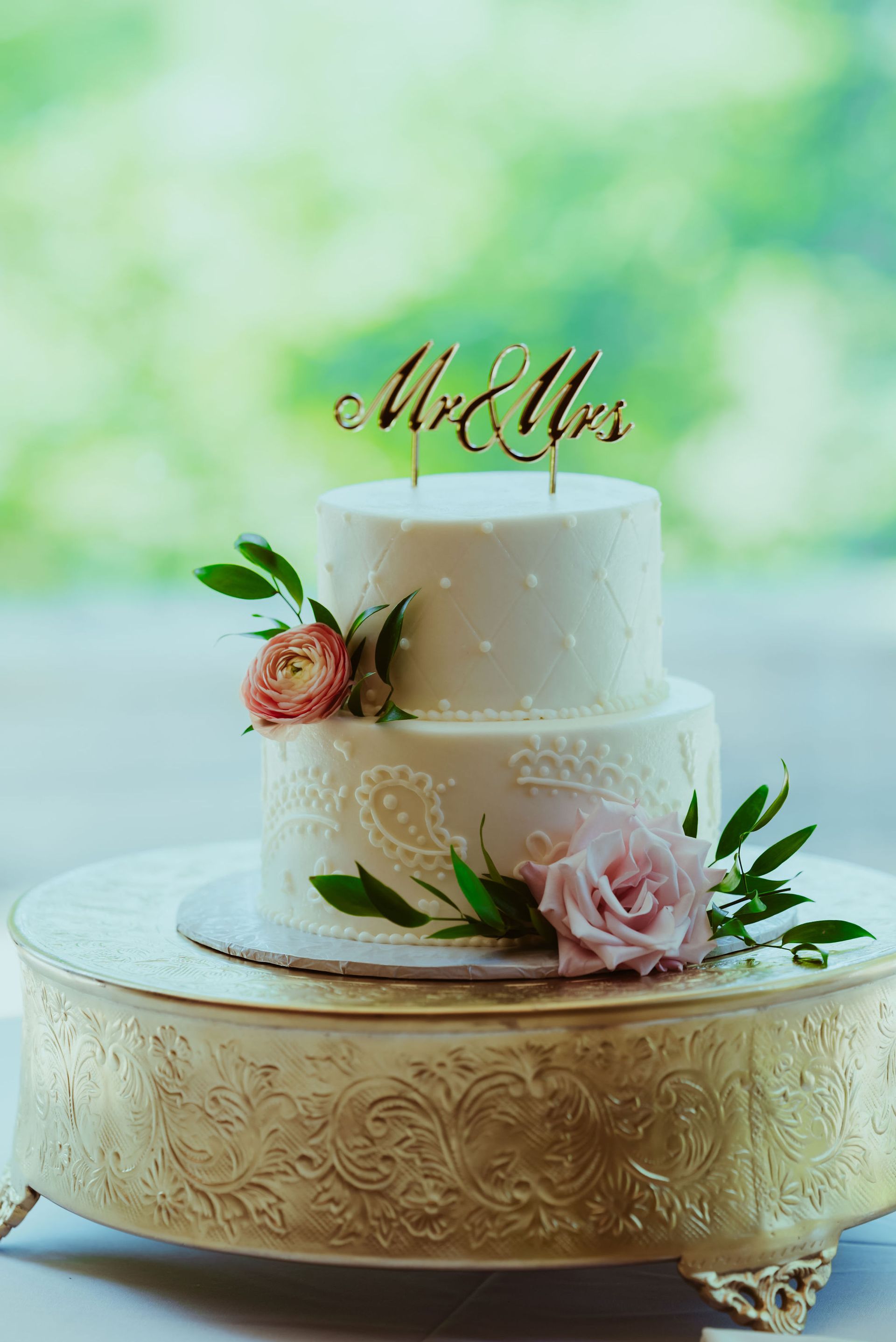 A wedding cake is sitting on top of a gold cake stand.