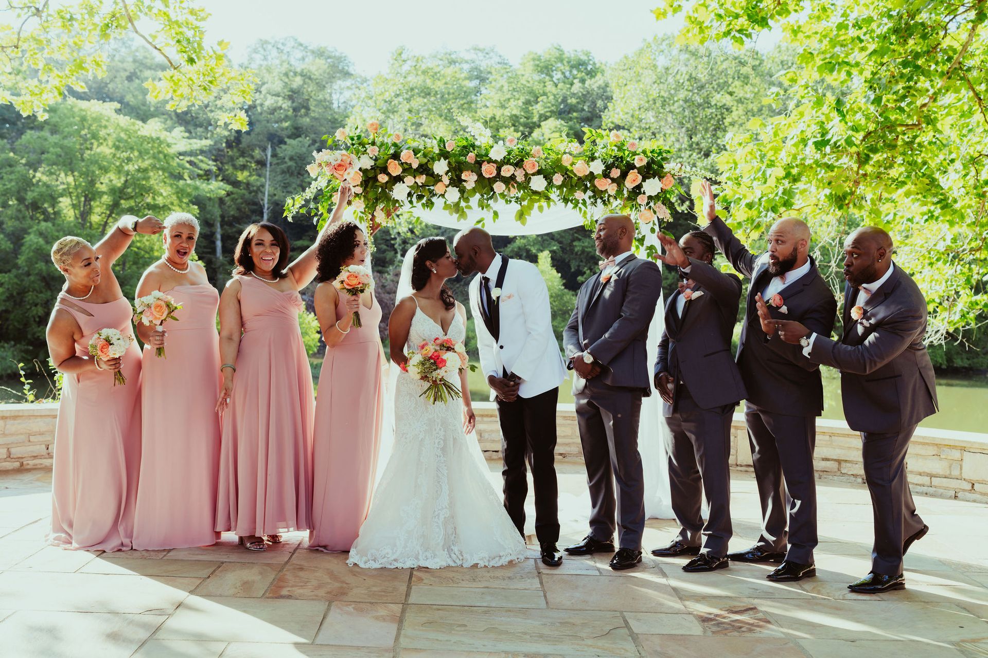 A bride and groom kissing in front of their wedding party.