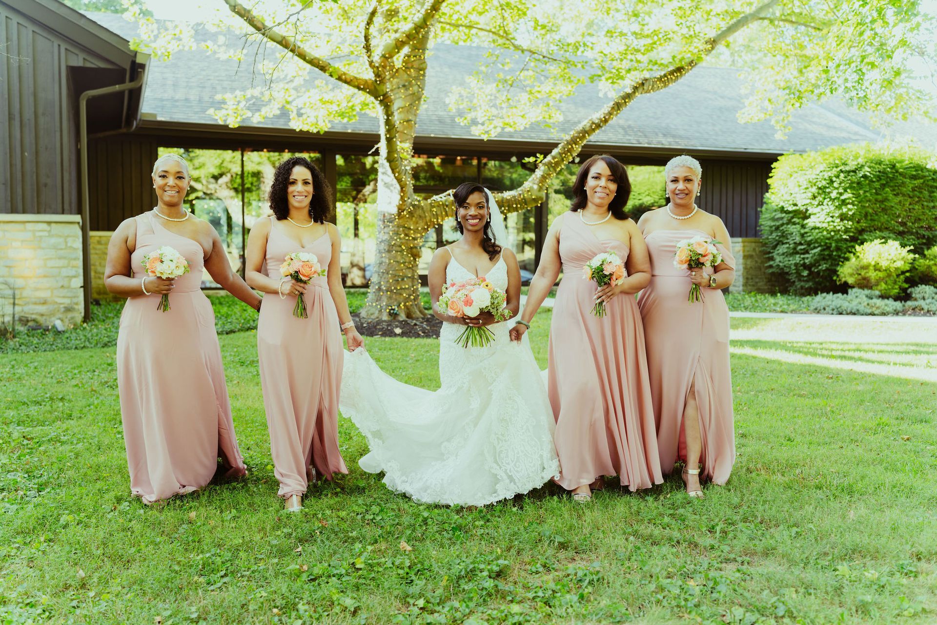 A bride and her bridesmaids are posing for a picture in the grass.