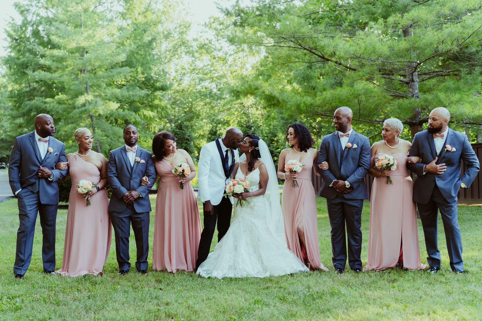 A bride and groom kissing in front of their wedding party.