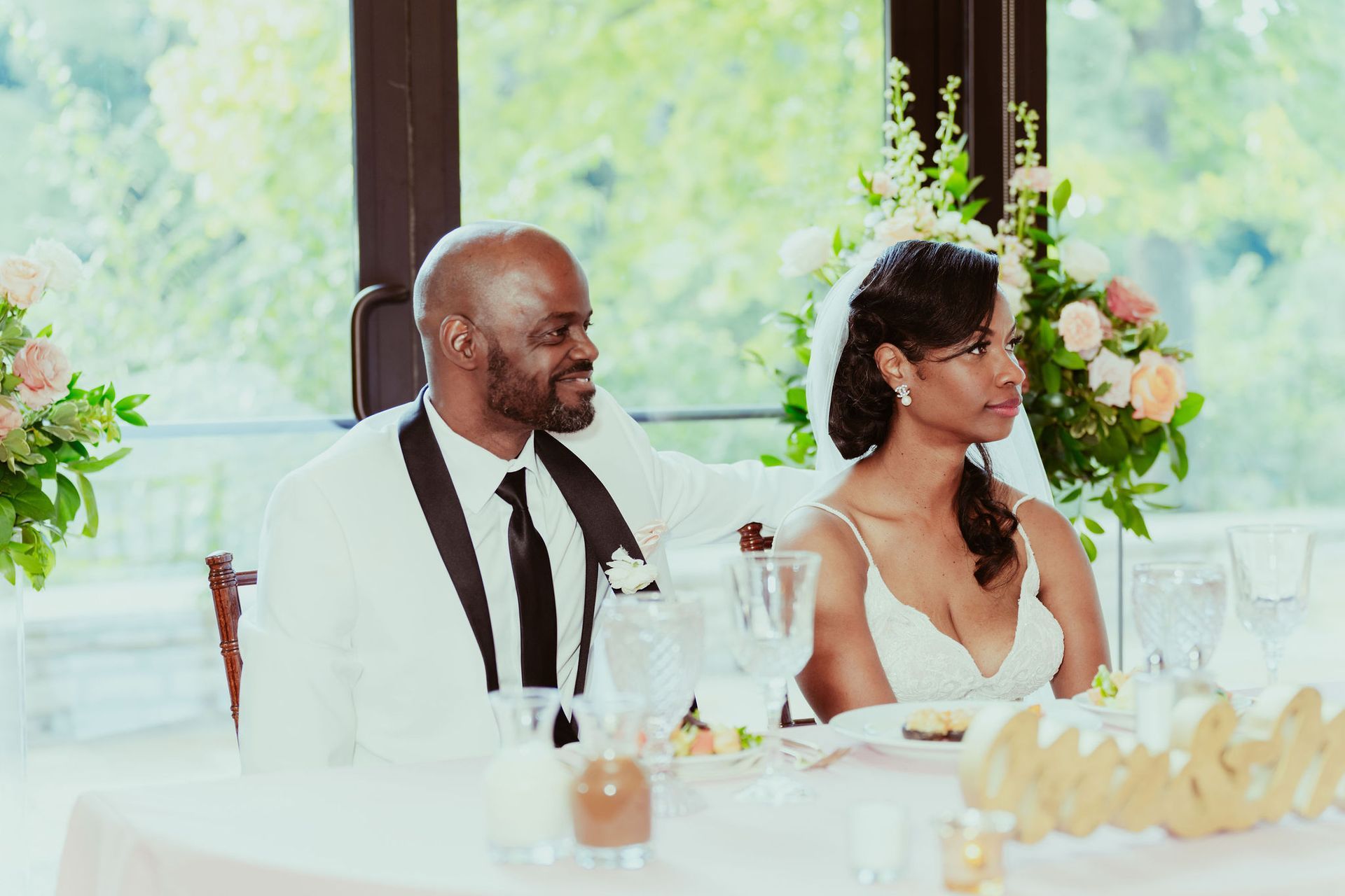 A bride and groom are sitting at a table at their wedding reception.