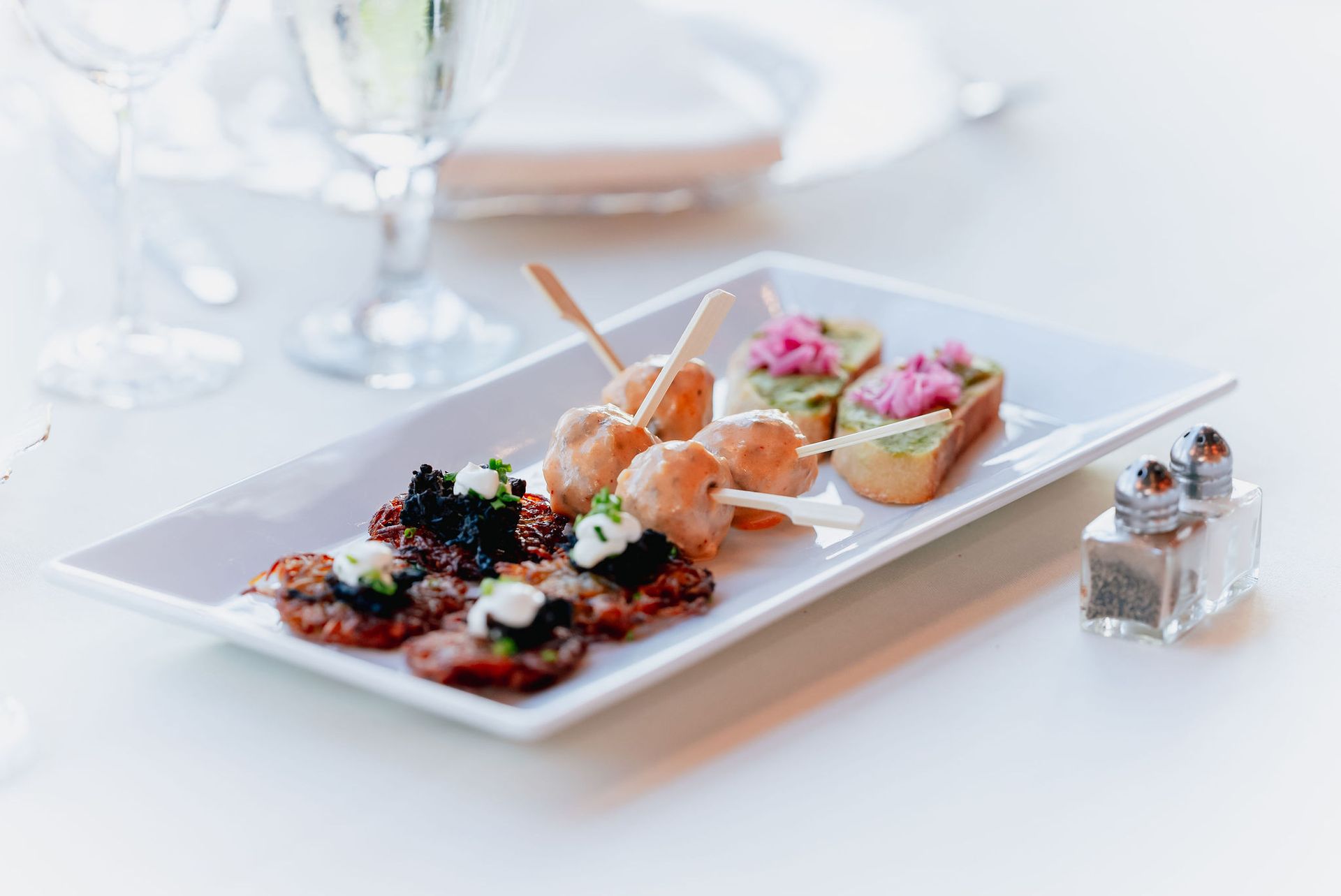 A white plate topped with appetizers and a salt and pepper shaker on a table.