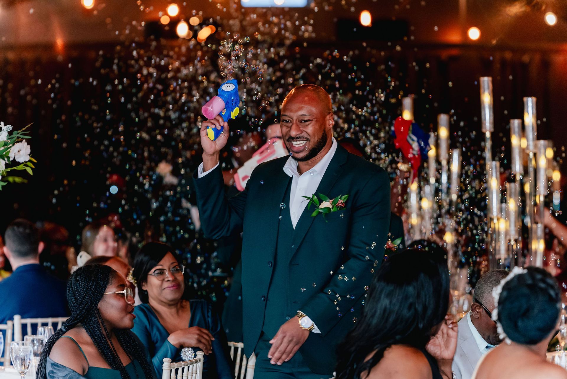 A man in a suit is standing in front of a crowd of people at a wedding reception.