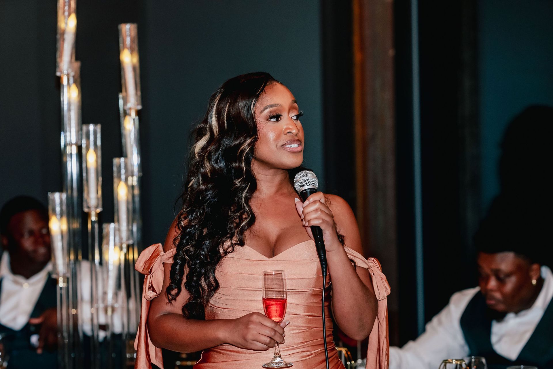 A woman in a dress is holding a glass of wine and a microphone.