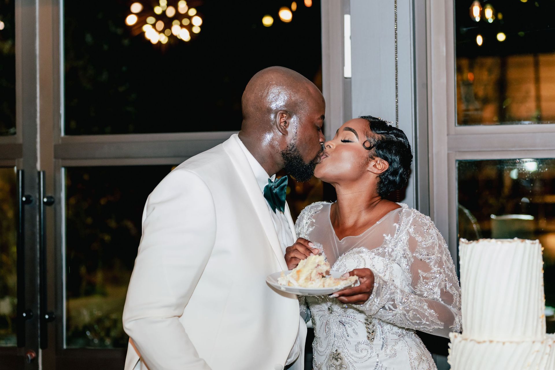A bride and groom are kissing after cutting their wedding cake.