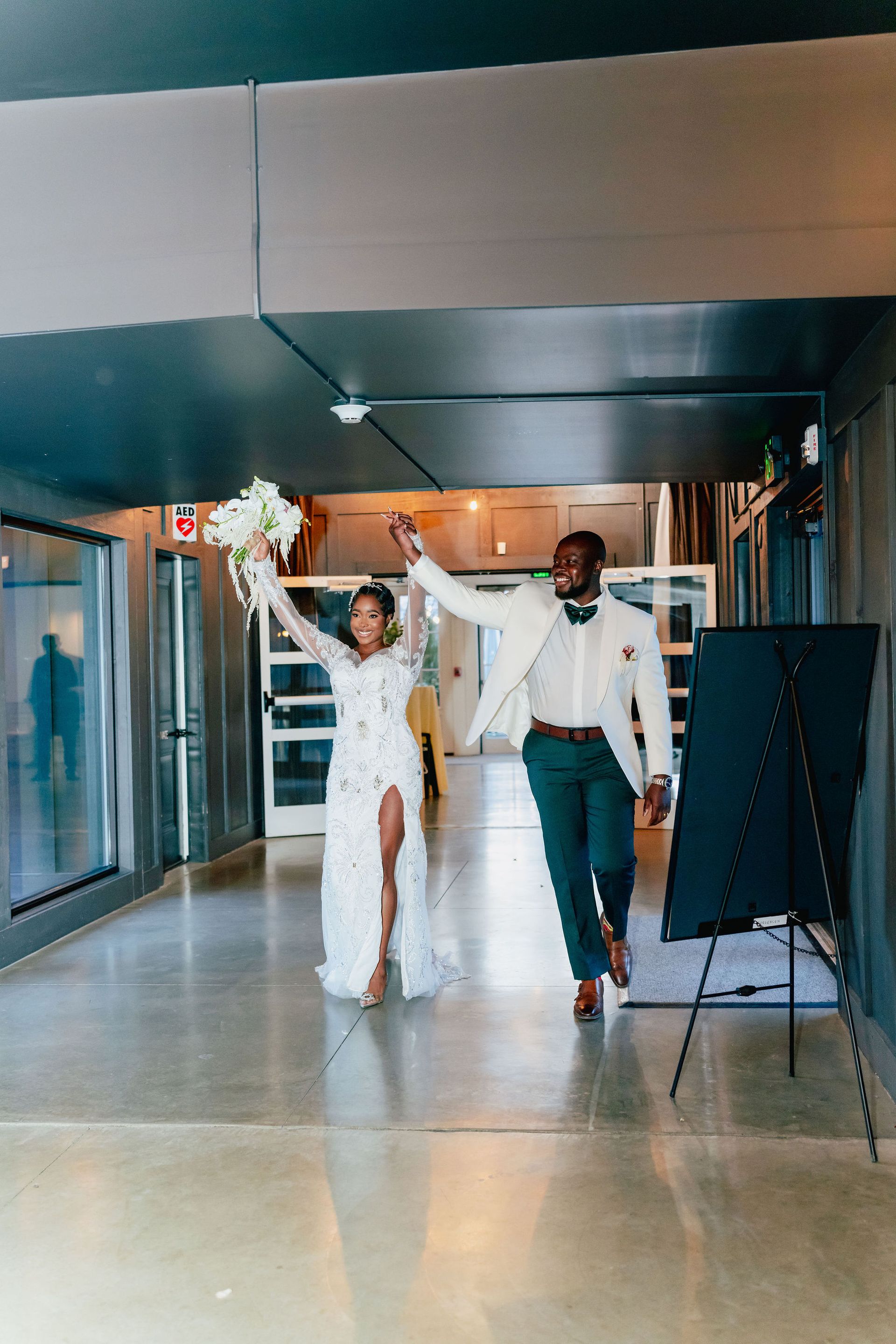 A bride and groom are walking down a hallway holding hands.