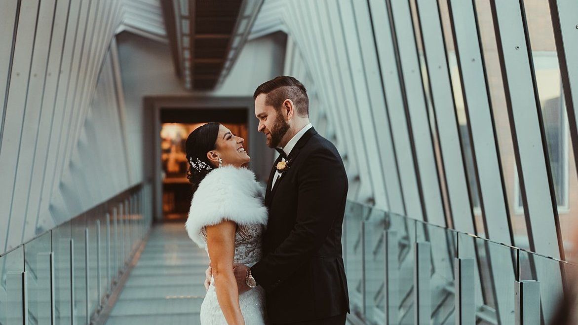 a bride and groom are standing next to each other on a bridge .