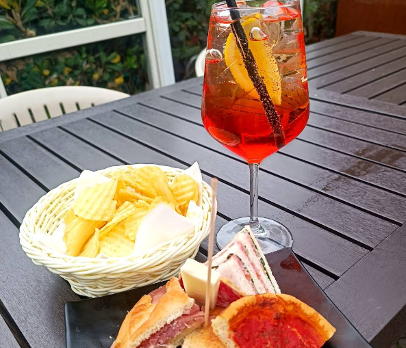Un cocktail Aperol Spritz e degli stuzzichini su un tavolo buio all'aperto. Patatine e panini in un cestino.