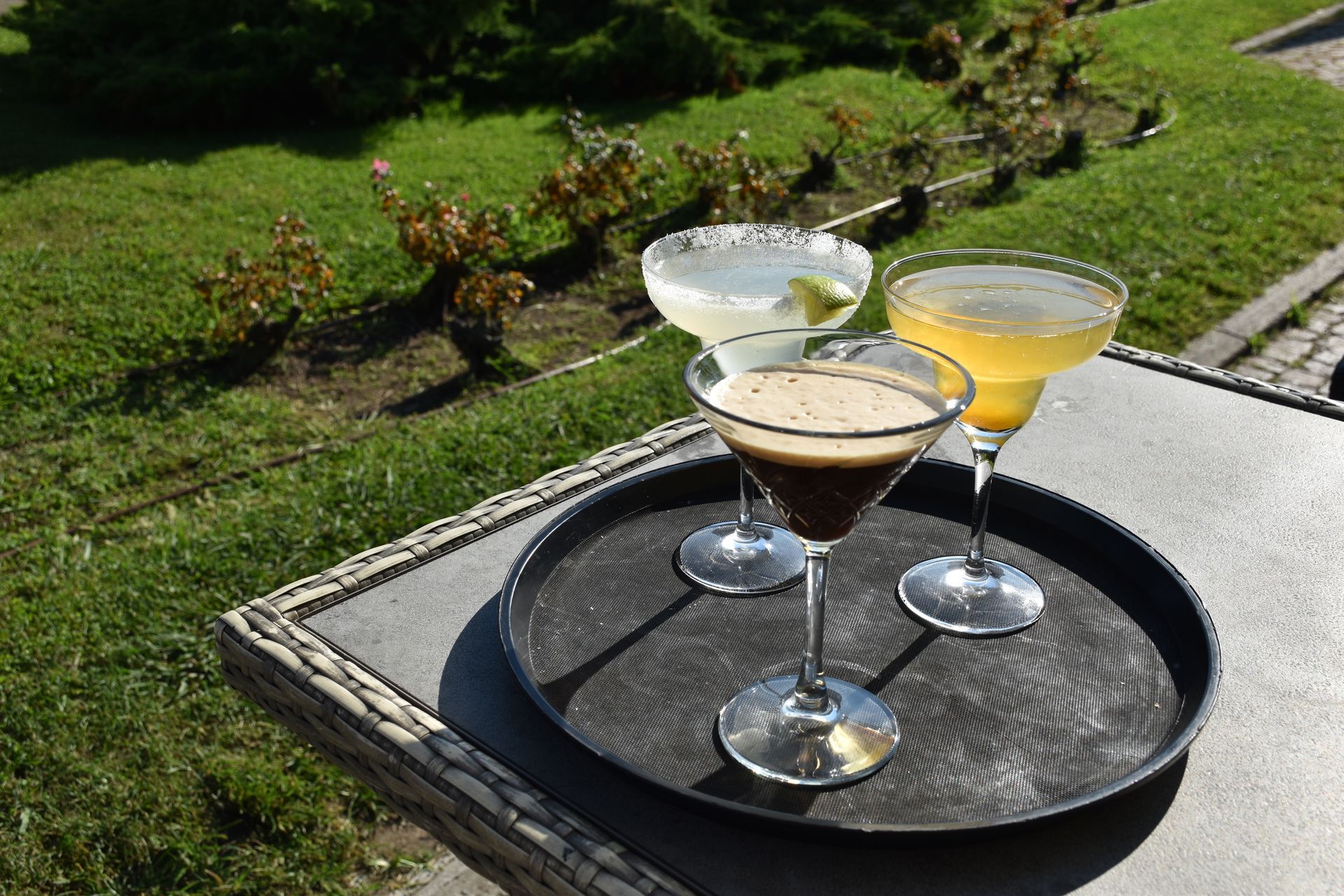 Tre cocktail su un vassoio all'esterno: una margarita, un espresso martini e un drink giallo.