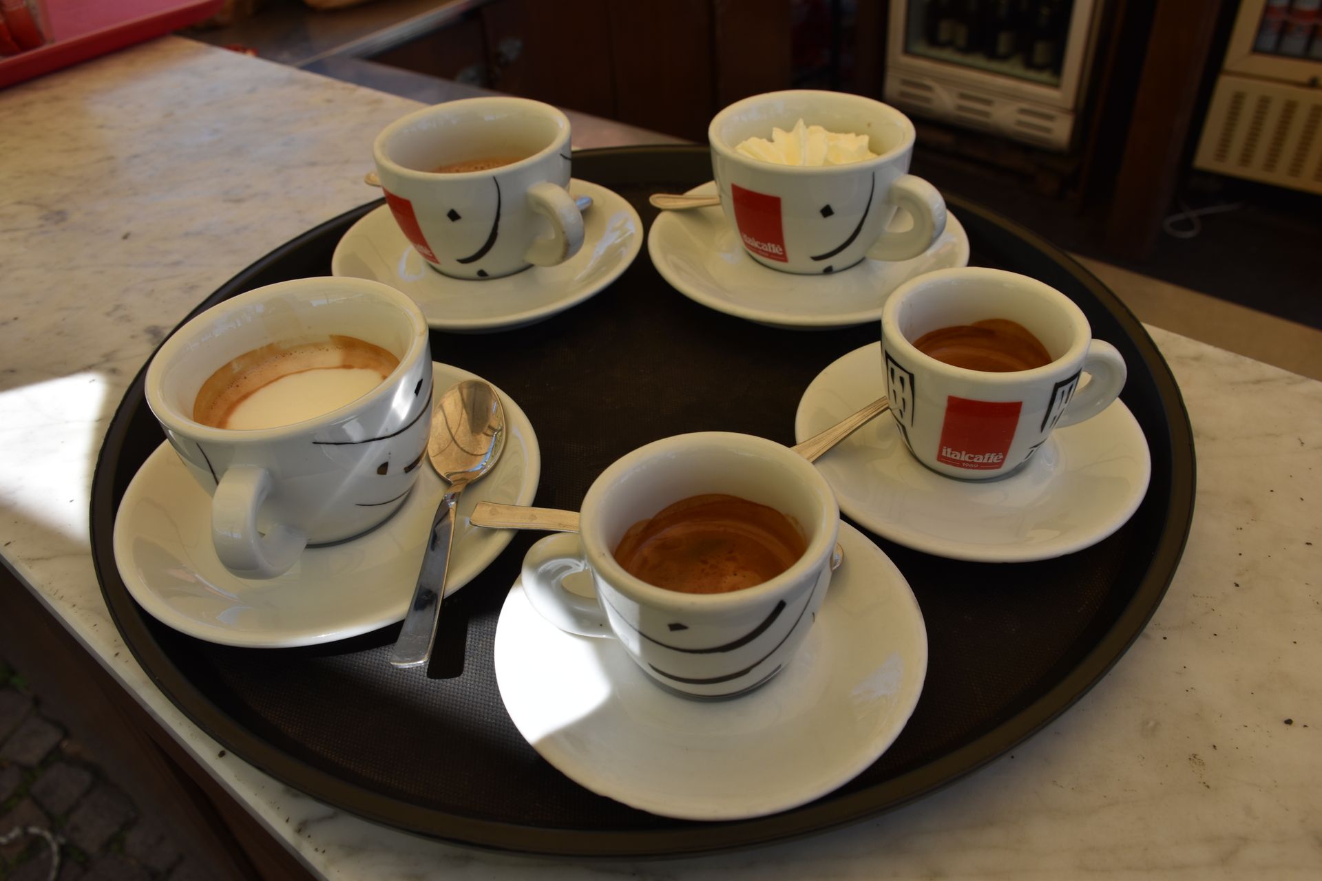 Vassoio di tazze da caffè: espresso, cappuccino, tè ed espresso con panna montata, su un piano di marmo.