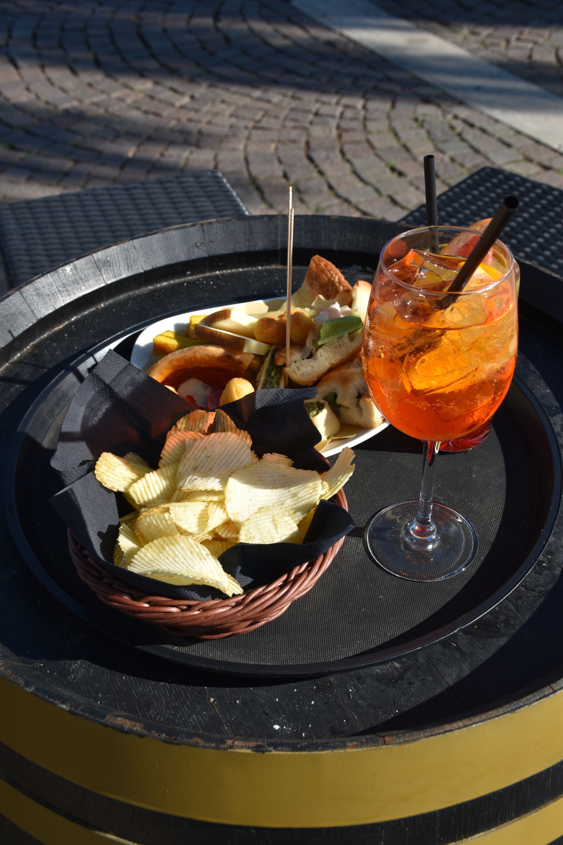 Uno spritz Aperol con stuzzichini su un tavolo rotondo all'aperto.
