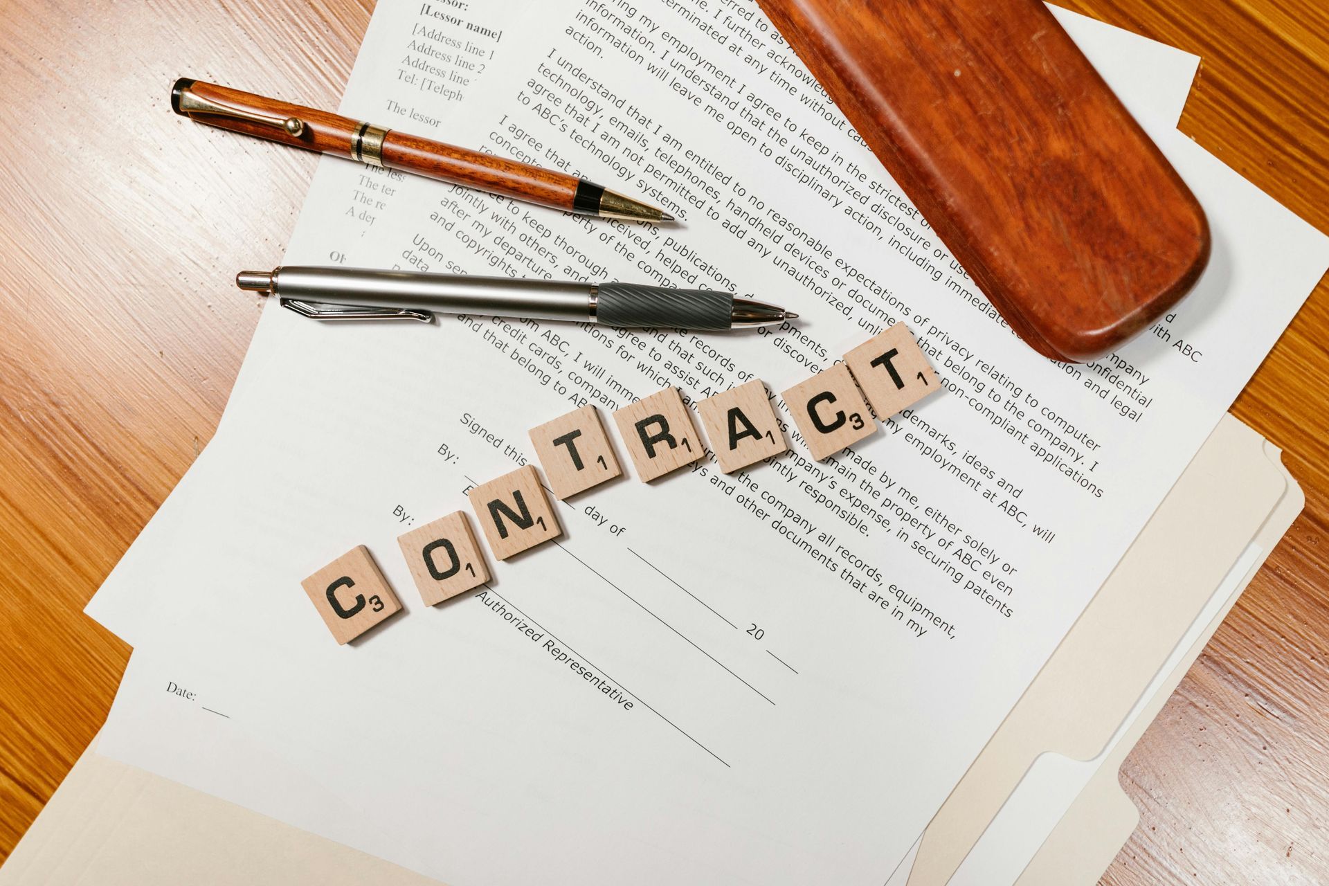 Scrabble tiles spelling “CONTRACT” on legal papers beside a pen and glasses