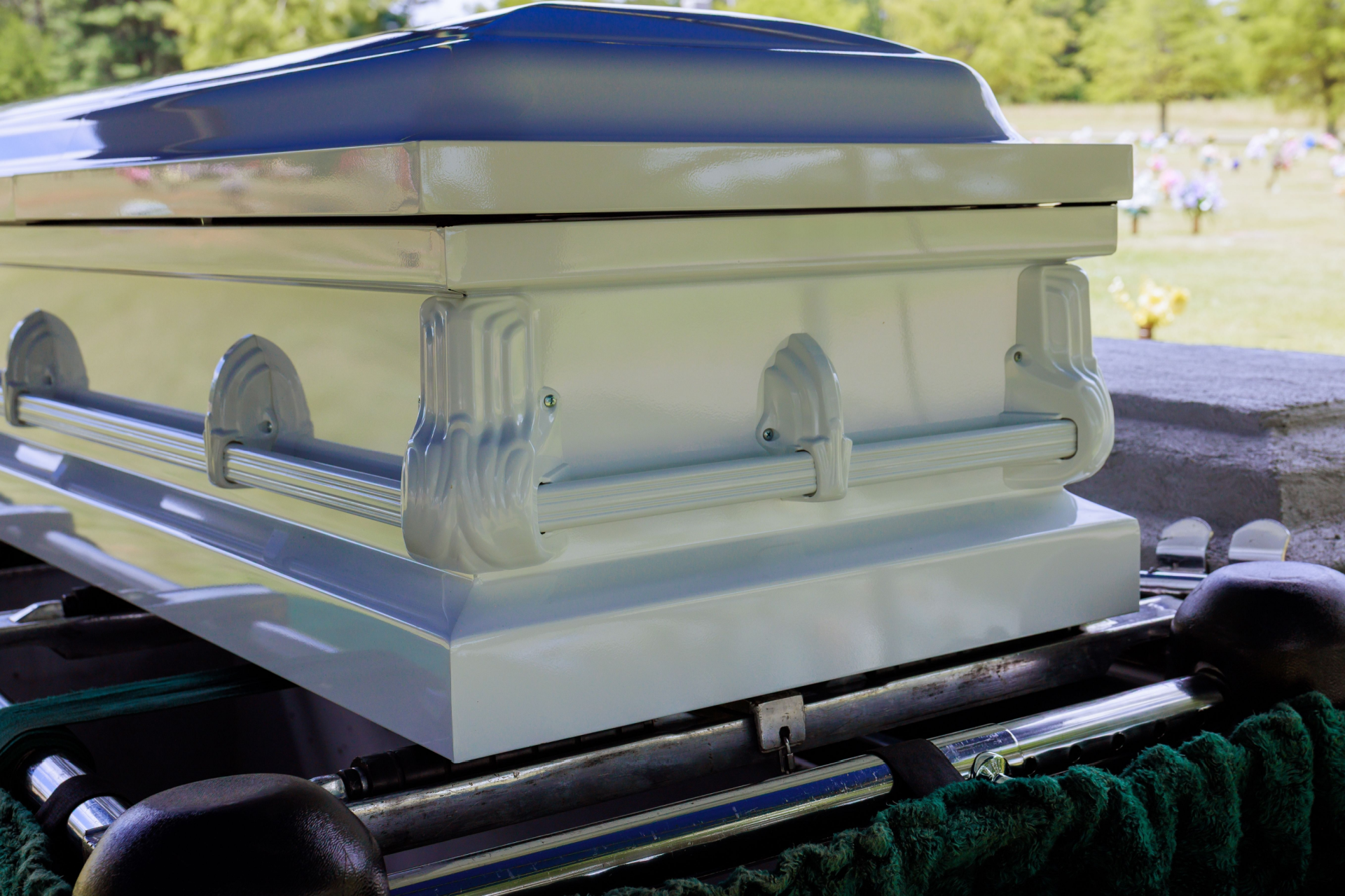 Light blue coffin at a graveside service, with handles and onlookers in the background.