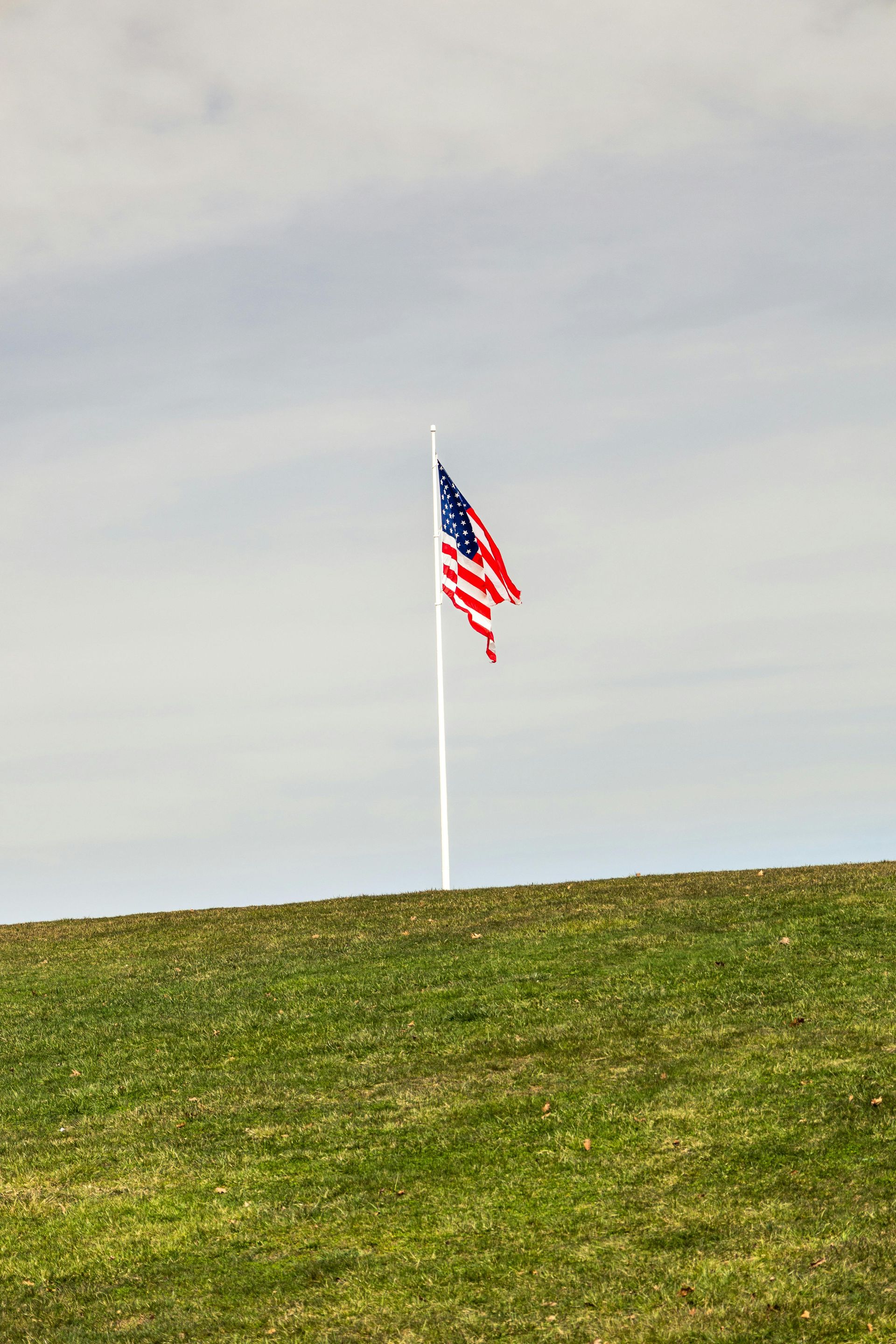 Brick pathway leading to a weathered wooden house with an American flag; buildings flank sides.