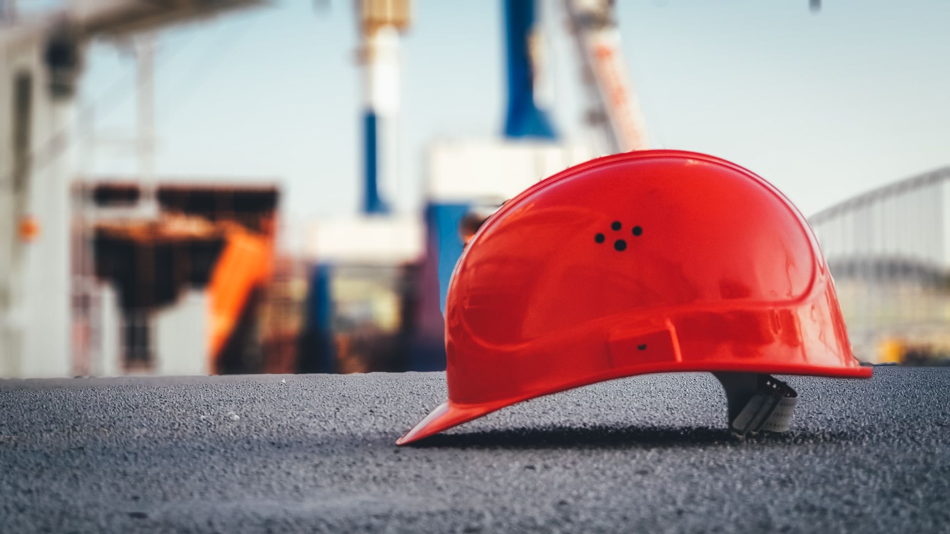 A red hard hat is sitting on the ground in front of a construction site.