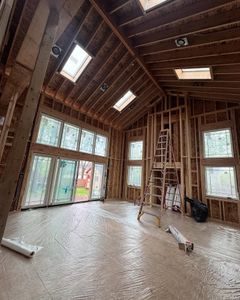 Interior of a wood-framed building under construction with windows and skylights. A ladder leans against the wall.