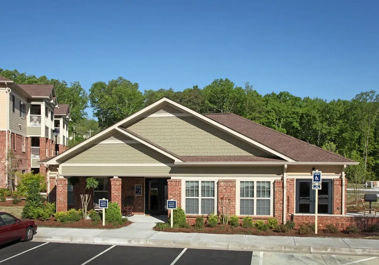Leasing office with brick columns and a gabled roof; front parking lot with a handicap-accessible spot.