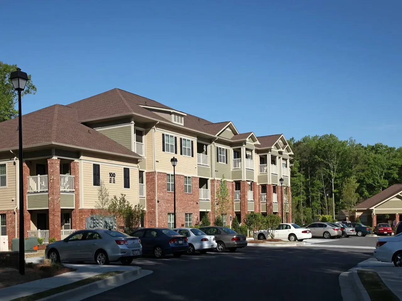 Exterior view of a multi-story apartment building with brick accents and a parking lot.
