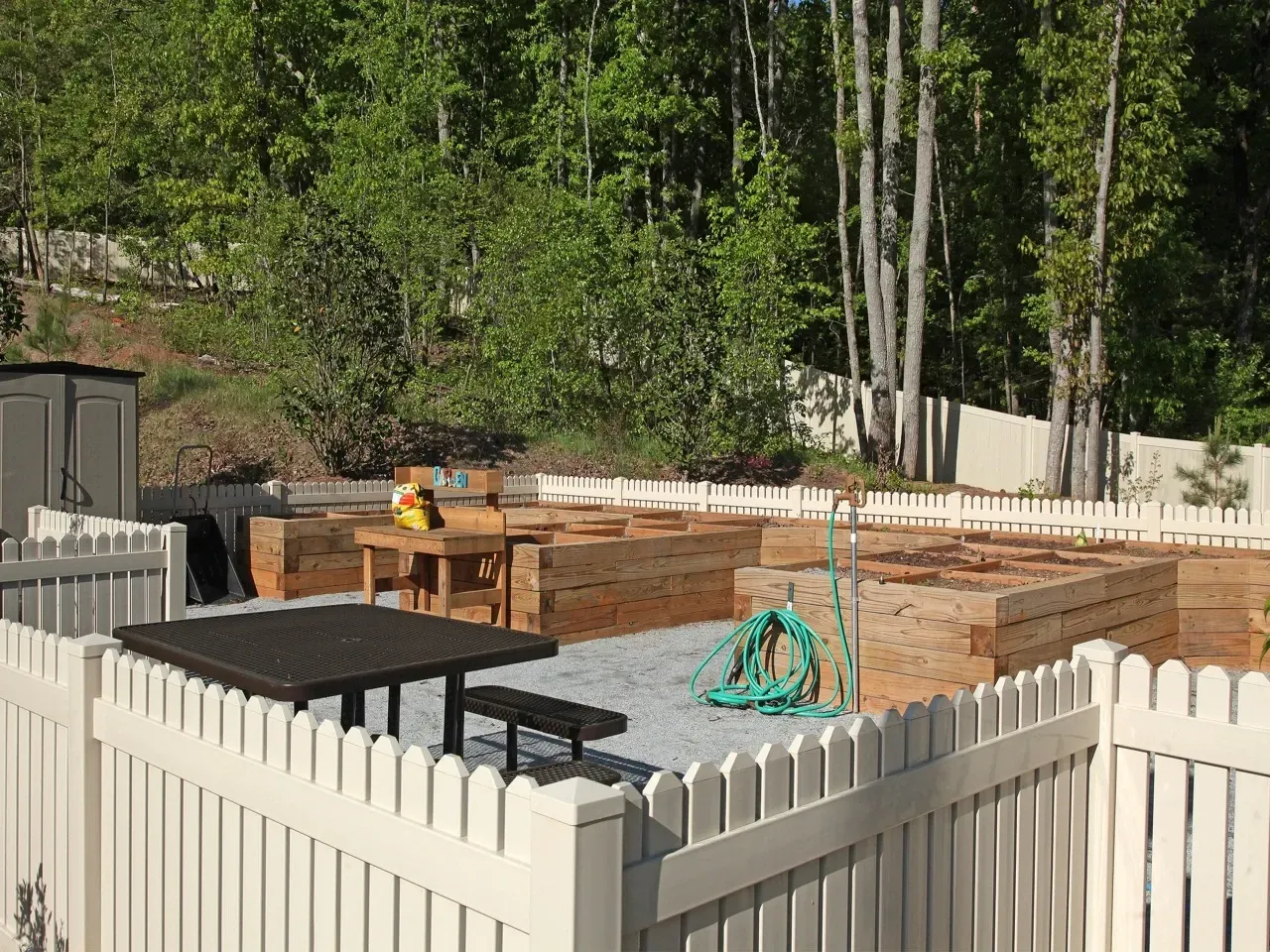 Outdoor community garden area with raised wooden planters and white fencing.