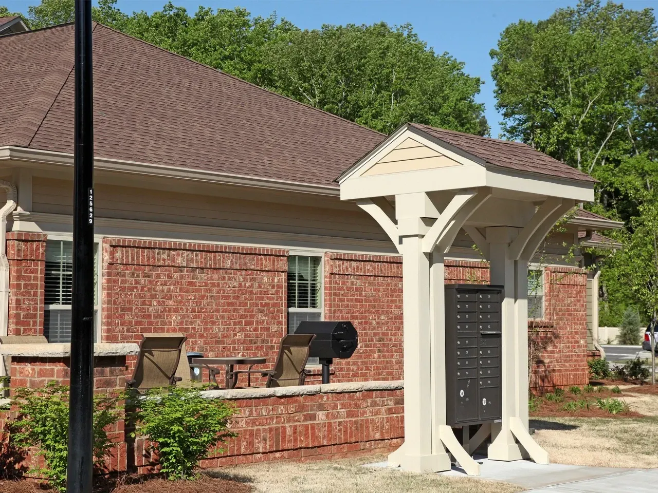 Brick apartment exterior with a communal mailbox shelter and outdoor seating.