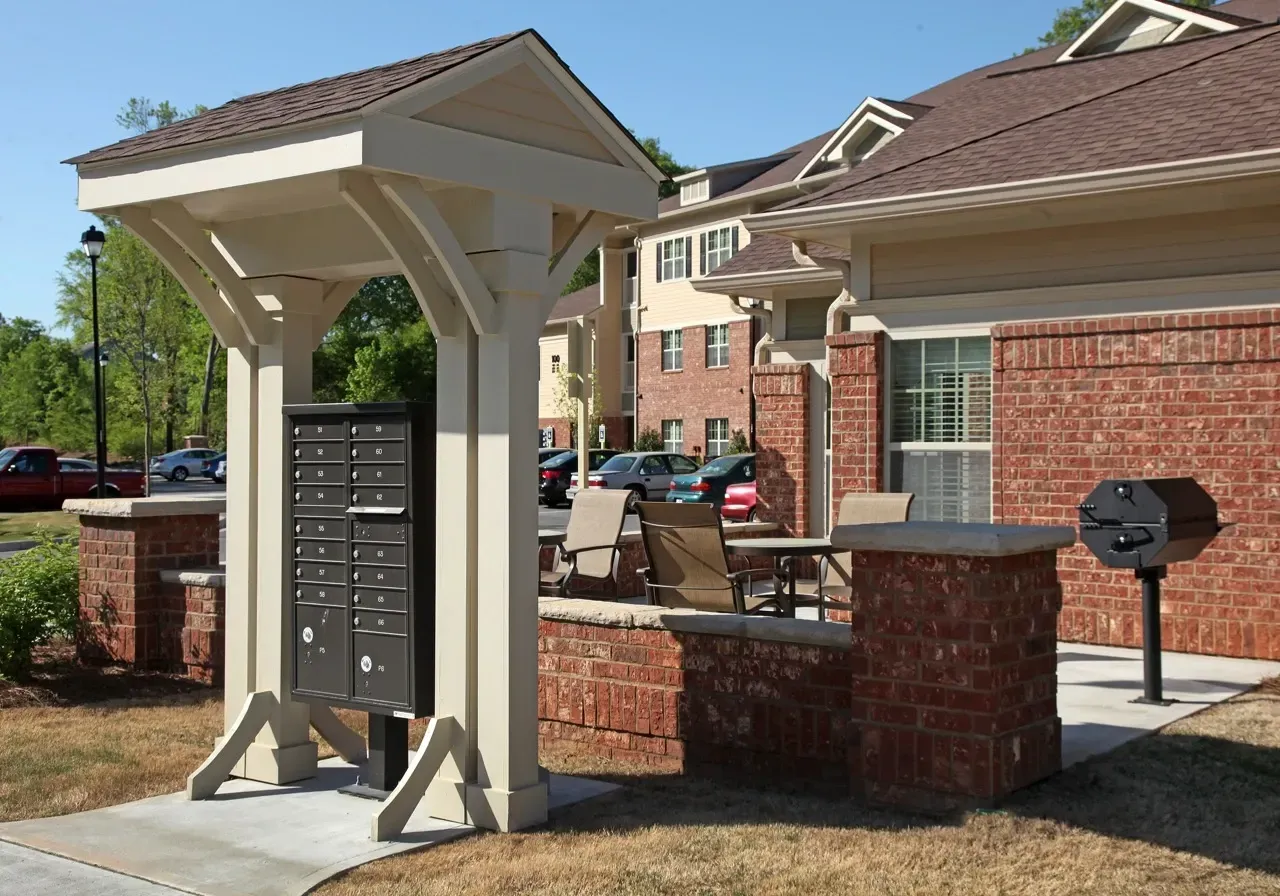 Exterior community courtyard with mailboxes, seating area, and a brick grill beside the building.