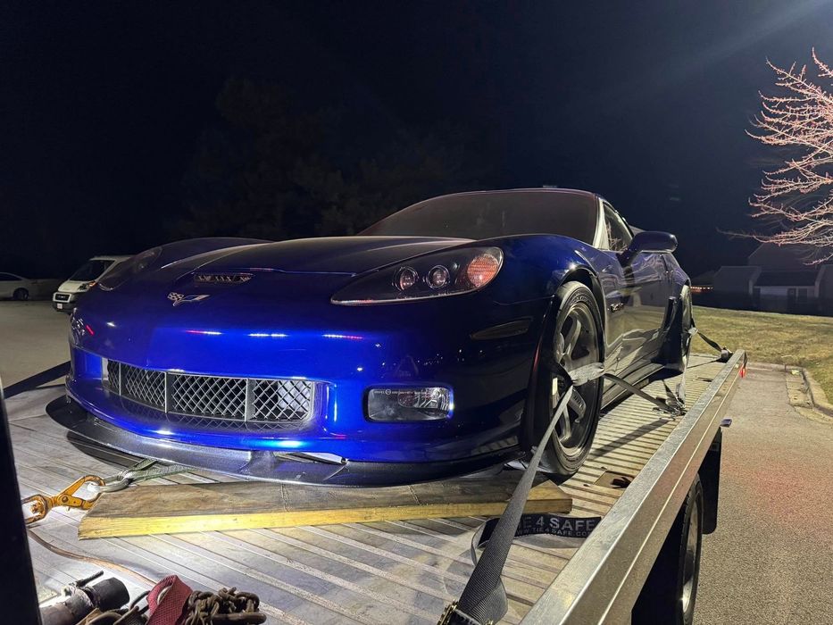 Blue Corvette sports car secured on a flatbed tow truck at night.